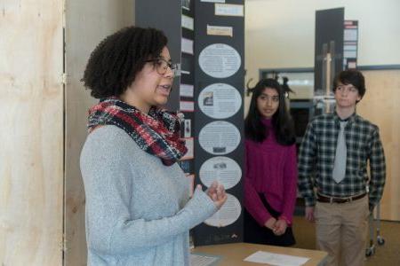 Three students present their NHD exhibit board.  One student in the foreground is speaking to someone out of the photo.